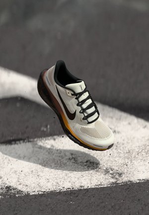 Weißer und schwarzer Nike-Laufschuh mit oranger Sohle in der Luft über einer Asphaltstraße mit weißen Markierungen.