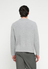 Lysegrå ribbestrikket genser med lange ermer, rund hals og avslappet passform, laget av teksturert strikket stoff.