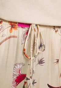 Blommönstrat beige tyg med snörning i midjan. Har färgglada blomdetaljer i orange, rosa och lila. Mjuk textur.