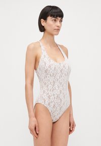 Lace badedragt i lys pink med scoop halsudskæring, brede stropper og blomstermønster, med en tætsiddende silhuet og højt skårne ben.