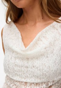 Robe en dentelle blanche avec un décolleté drapé, des motifs floraux délicats et un tissu texturé. La conception est ajustée avec des détails superposés.