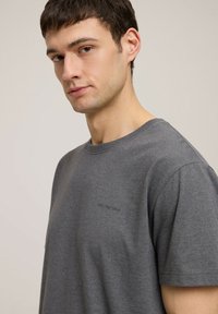 Szara bawełniana koszulka z okrągłym dekoltem, krótkimi rękawami i małym detalem logo na piersi. Gładka tekstura i luźny krój.