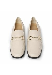 Mocasines de cuero color beige con un acabado suave, que presentan un detalle de cadena dorada en la parte frontal, punta redondeada y suela negra contrastante.