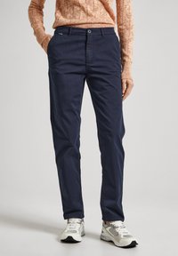 Marineblå chinos laget av lett stoff, med rett snitt, knappelukking og sidelommer. Kombinert med grå sneakers.