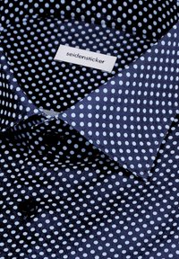 Camicia blu navy con superficie testurizzata, caratterizzata da un motivo a pois bianchi. Include un'etichetta con il marchio "seidensticker" vicino al colletto.
