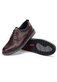 Zapatos de cuero marrón con una textura suave y detalles de costura. Presentan una suela de goma con un agarre estampado y acentos en contraste.