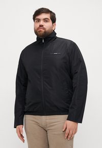 Giacca nera con zip realizzata in materiale liscio e leggero, con colletto alto, polsini elastici e un piccolo logo sul petto.