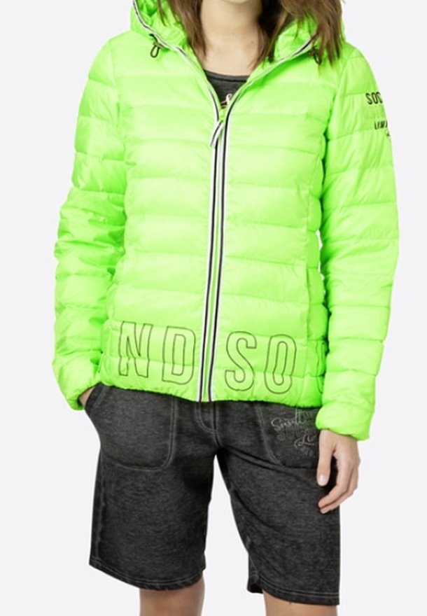 Giacca a vento verde neon con cuciture orizzontali, chiusura con zip e cappuccio. Abbinata a pantaloni corti grigi scuri con cuciture decorative.