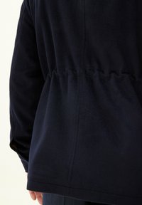 Takkameren sininen fleece-takki, jossa on kerätty vyötärö, hieno tekstuuri ja hienovaraiset ompelu-yksityiskohdat selässä ja hihoissa.