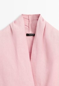 Lichtroze linnen kledingstuk met een sjaalkraag en een zichtbaar zwart label met de tekst "Massimo Dutti" genaaid aan de binnenkant van de halslijn.