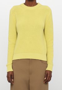 Maglione giallo lavorato a maglia con texture a coste, collo a giro e maniche lunghe. Vestibilità leggermente rilassata, abbinato a pantaloni beige.
