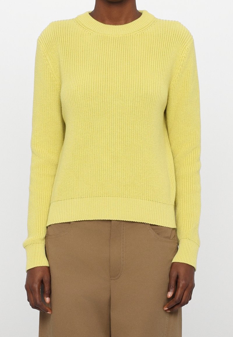 Maglione giallo lavorato a maglia con texture a coste, collo a giro e maniche lunghe. Vestibilità leggermente rilassata, abbinato a pantaloni beige.