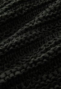 Czarna, teksturowana tkanina z plecionym wzorem, charakteryzująca się miękkim, wplecionym wyglądem oraz zmienną grubością przędzy.