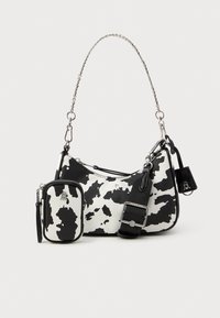 Bolso de mano con estampado de vaca en blanco y negro, con una cadena plateada, que cuenta con un mini bolso extraíble y un exterior liso y texturizado.