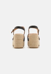 Sandalias negras texturizadas con una correa de hebilla y tacones de bloque de yute enrollado. La plantilla es de tono nude con un diseño acolchado para mayor comodidad.