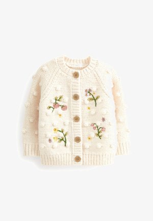 Cardigan pour bébé tricoté en crème avec boutons en bois, boucles texturées, et fleurs brodées rose, jaune et violettes sur le devant.