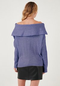 Pulover s širokimi rameni v vijolični barvi z rebrasto strukturo in dolgimi rokavi, ki ima širok ovratnik in teksturirano pletenje, v kombinaciji s črno usnjeno mini krilo.