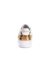 Sneaker bianchi con un accento in metallo dorato sul tallone. Presentano un design pulito e semplice, con una linguetta sul tallone brandizzata con la scritta "GUESS" in lettere dorate.