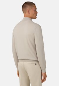 Šviesiai rudas, lengvas megztinis su aukštu apykakle, raukšlėtomis rankogaliais ir apačia. Lygus audinys, prigludusi forma. Dėvimas su šviesios spalvos kelnėmis.