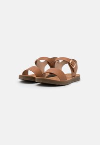 Tan leather sandals with two wide straps and a buckle. The sole is flat and textured, providing a casual design suitable for warm weather.