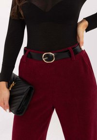 Bordowe sztruksowe spodnie z czarnym skórzanym paskiem z okrągłą złotą klamrą, zestawione z czarną pikowaną torebką kopertową.