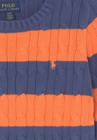 Pletený svetr s modro-oranžovými vodorovnými pruhy, s žebrovaným výstřihem a malým vyšitým logem na hrudi.