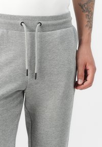 Gray sweatpants featuring a drawstring waistband, ribbed texture, and side pockets. Close-up view of fabric and hand holding the waistband.