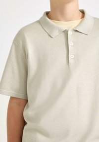 Ljusbeige polo shirt i texturerad tyg, med klassisk krage och tre knappslå. Kort ärm.