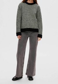 Zwart- en grijsgebreide trui met chevronpatroon en een zwarte zoom, gecombineerd met grijze jeans met wijde pijpen en zwarte enkellaarsjes.