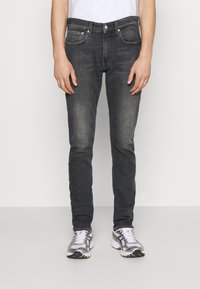 Mörkgrå denimjeans med slim fit, femfickorsdesign och subtil nedtoning. Matchas med silverfärgade och vita sportskor.
