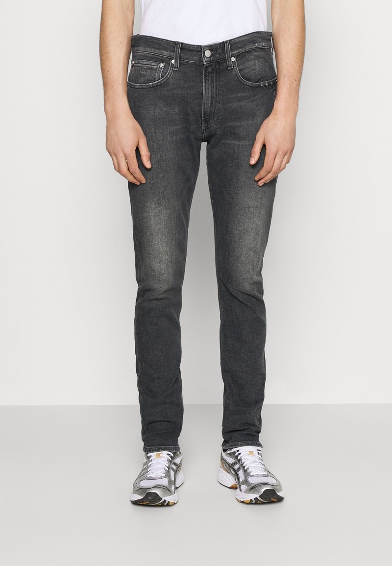 Mörkgrå denimjeans med slim fit, femfickorsdesign och subtil nedtoning. Matchas med silverfärgade och vita sportskor.
