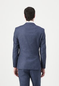 Mėlynas tekstūruotas švarkas su pritaikytu siluetu, vienu ventiliacijos atidarymu gale ir sagčių rankovėmis. Kelnės atitinka švarko spalvą ir medžiagą.