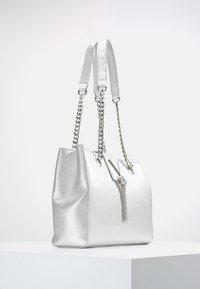 Silverfärgad handväska med strukturerad yta, dubbla handtag, kedjedetalj och tofs. Har en strukturerad form och metallisk lyster.