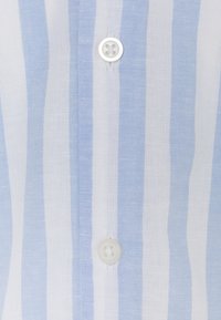 Pionowy, niebiesko-biały materiał w paski z dwoma białymi guzikami wszytymi w pionowej linii na koszuli.