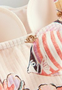 Gros plan sur des bonnets de soutien-gorge rembourrés couleur crème avec une bretelle en tissu beige présentant un motif à rayures multicolores et floraux ainsi qu'une petite boucle métallique ronde.