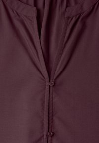 Gros plan de l'avant d'une chemise grenat avec un col en V et deux boutons assortis visibles sur un tissu lisse.