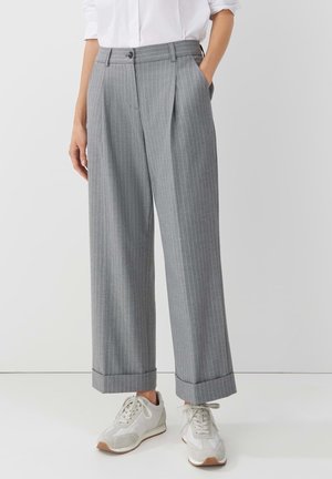 Pantalones anchos de rayas grises con bajos doblados combinados con zapatillas blancas y una camisa blanca por dentro.