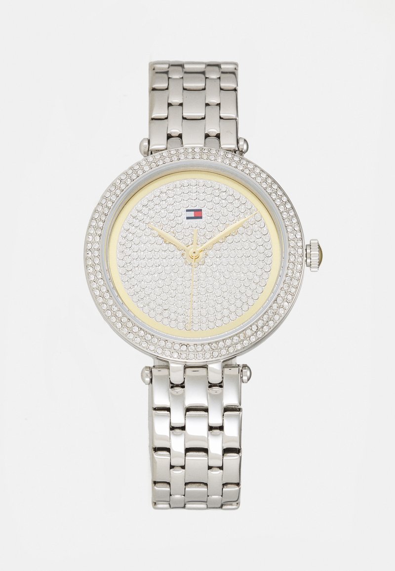 Reloj plateado con esfera redonda, adornado con cristales, acentos amarillos y una correa de pulsera metálica. Presenta manecillas doradas y logo.