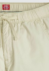 Lichtbeige chinos met een elastische tailleband, binnenste trekkoord en een gladde textuur. Merkenlabel zichtbaar aan de bovenkant.