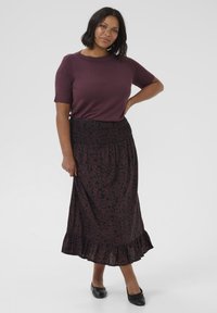 Top viola a maniche corte abbinato a una gonna maxi nera con motivo floreale e orlo arricciato. Calzature sono ballerine nere.