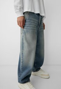 Helle blaue, weiter geschnittene Jeans aus Denim mit einem ausgewaschenen Finish, ausgestattet mit seitlichen Taschen und einem ausgefransten Saum, kombiniert mit weißen Sneakers.