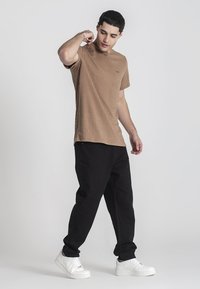 Bruine textuur korte mouw t-shirt, relaxte pasvorm, gecombineerd met zwarte broeken en witte sneakers. De outfit heeft een minimale merkuitstraling.