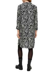 Schwarz-weißer gemusterter Hemdkleid mit mittellangem Design, langen Ärmeln und Kragen. Tragen mit schwarzen engen Leggings und Stiefeletten.