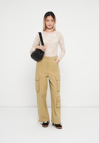 Beige cargo bukser med sidelommer, kombinert med en gjennomsiktig blonde langermet topp. En liten svart crossover-sekk kompletterer antrekket.