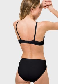 Black lingerie set features a smooth, stretchy fabric with adjustable straps and a hook closure. High-waisted design with scalloped trim detail.