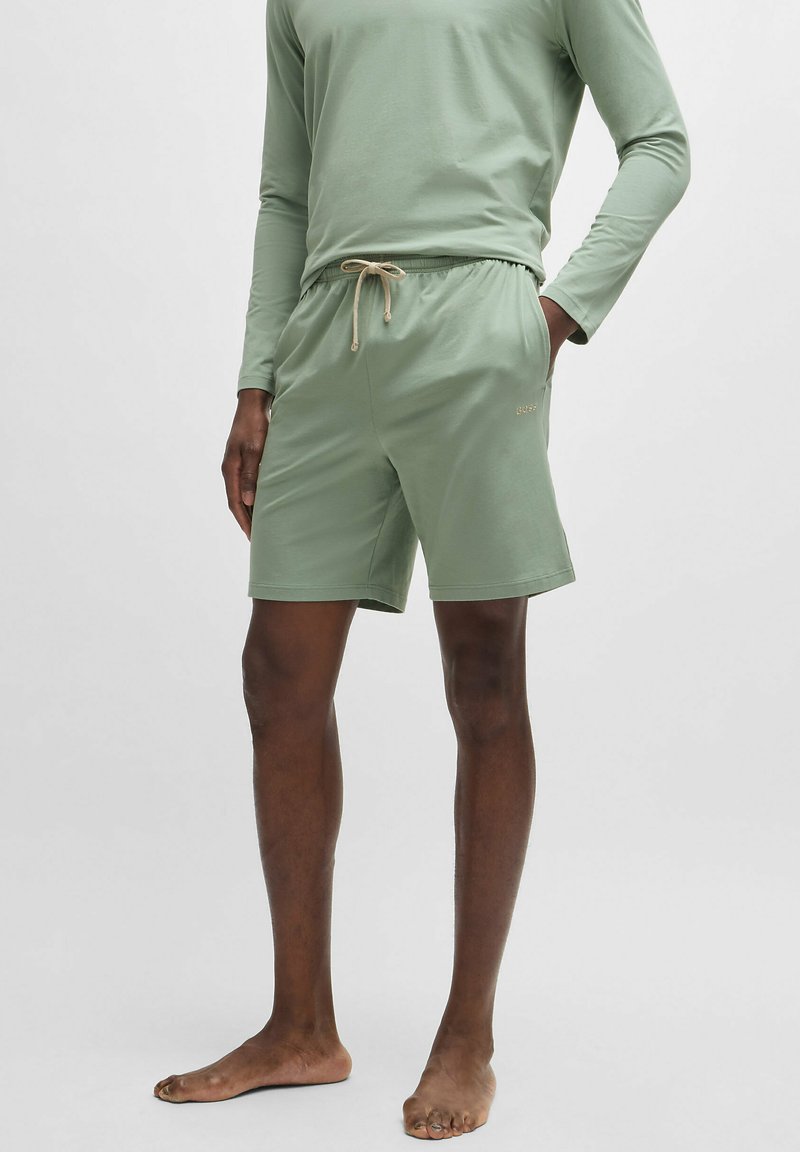 Lichtgroen shirt met lange mouwen en elastische tailleband aan de korte broek, voorzien van een beige trekkoord en een subtiel logo op de korte broek.