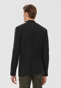 Czarna marynarka o zdefiniowanej sylwetce, jednorzędowa, z klapami i detalem przy mankietach w postaci trzech guzików. Gładki materiał i dopasowany krój.