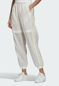 Vita lätta joggerbyxor med elastisk midja, sidofickor och beige ränder. Utrustad med logotypemblem och elastiska muddar. Bärs med vita sneakers.