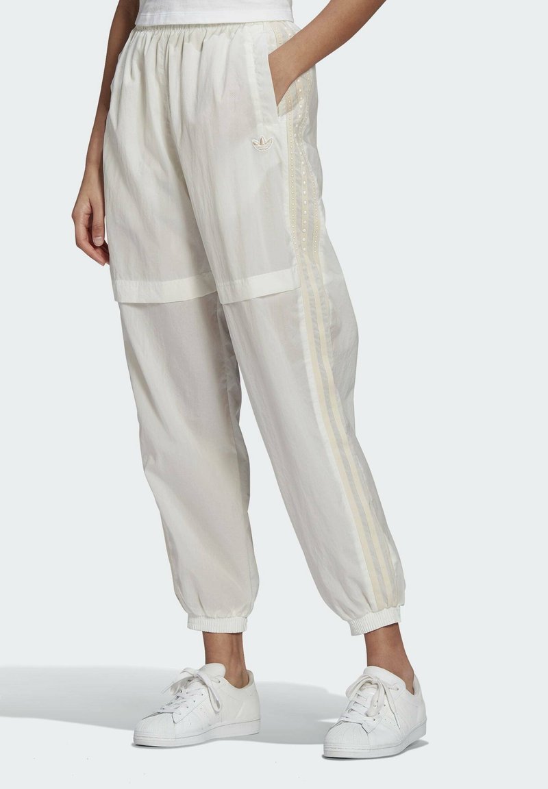Vita lätta joggerbyxor med elastisk midja, sidofickor och beige ränder. Utrustad med logotypemblem och elastiska muddar. Bärs med vita sneakers.