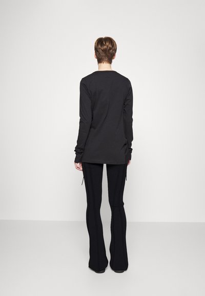 Camisa preta longa, feita de tecido suave, com um corte descontraído e mangas longas. Combinada com calças pretas de flared com texturas canalizadas.